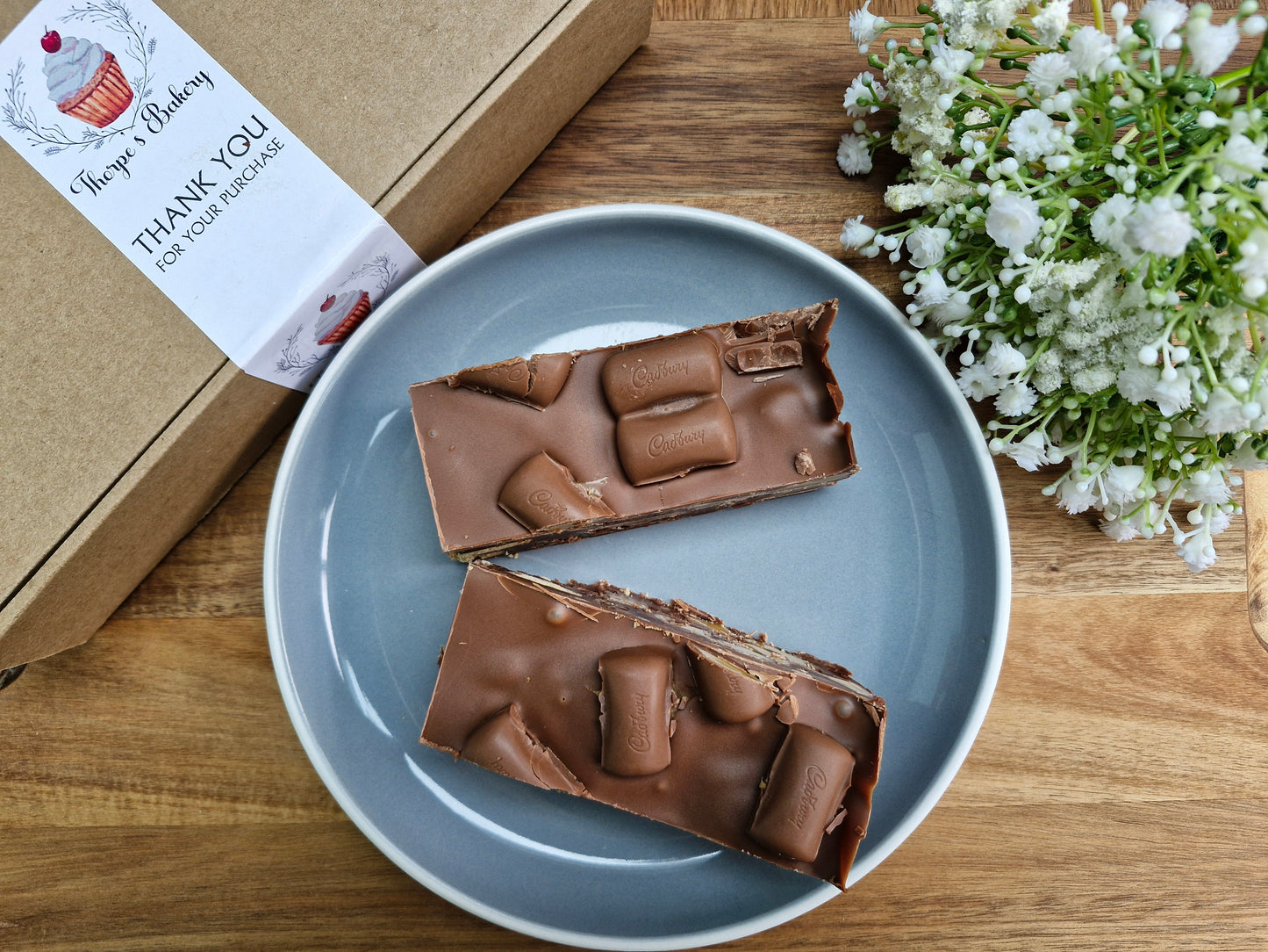 Two large cadbury caramel chocolate tiffin slices on a plate beside a Thorpe’s Bakery treat box.