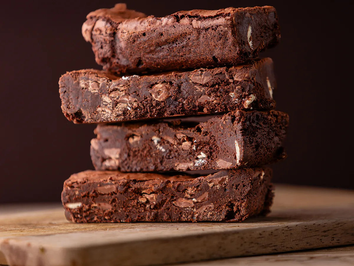 Two large rich brownie slices on a plate beside a Thorpe’s Bakery treat box on a rustic wooden surface.