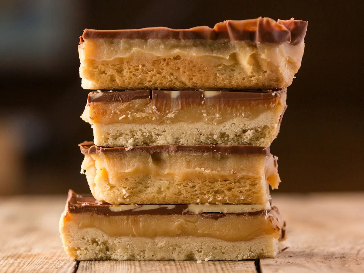 Two millionaire’s shortbread slices with marbled chocolate topping beside a Thorpe’s Bakery treat box.