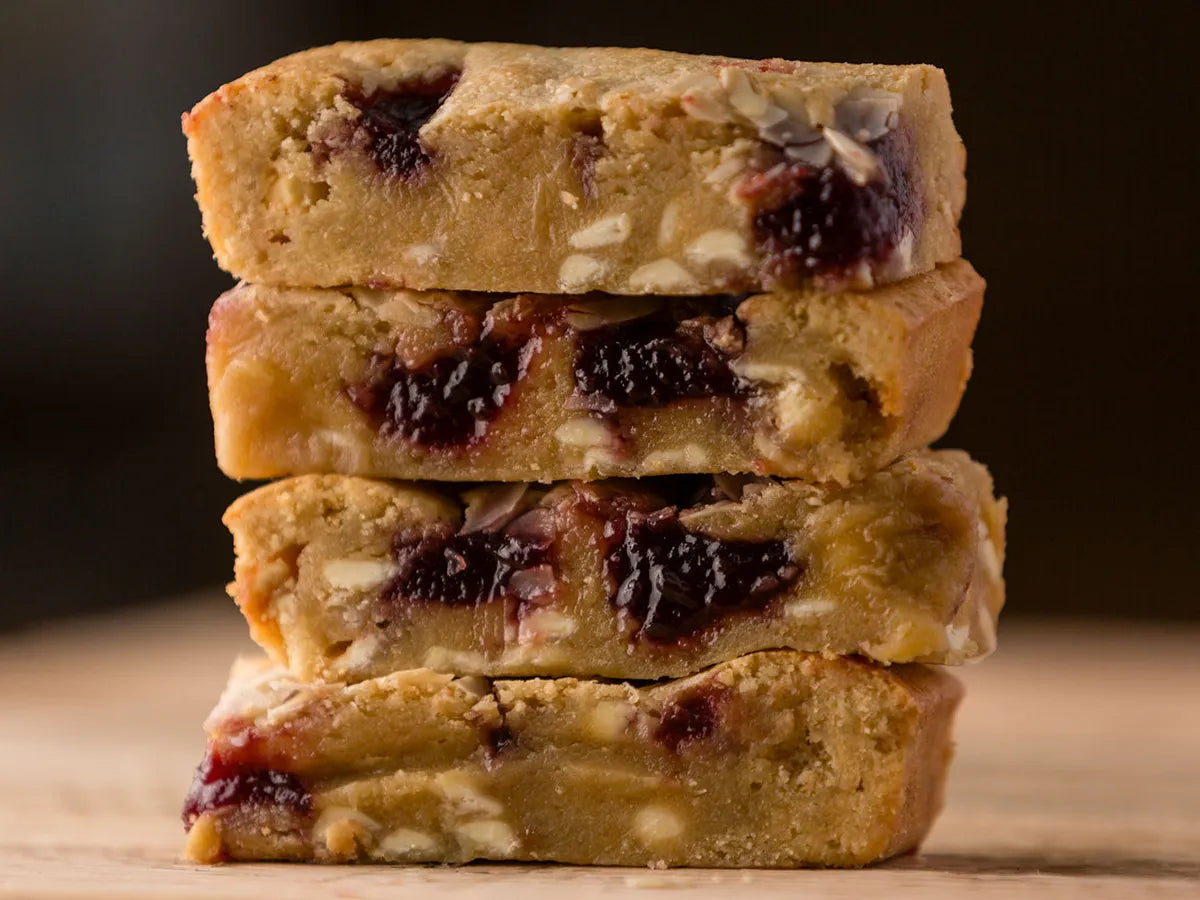 Two large Biscoff blondie slices on a plate beside a Thorpe’s Bakery treat box on a rustic wooden surface.