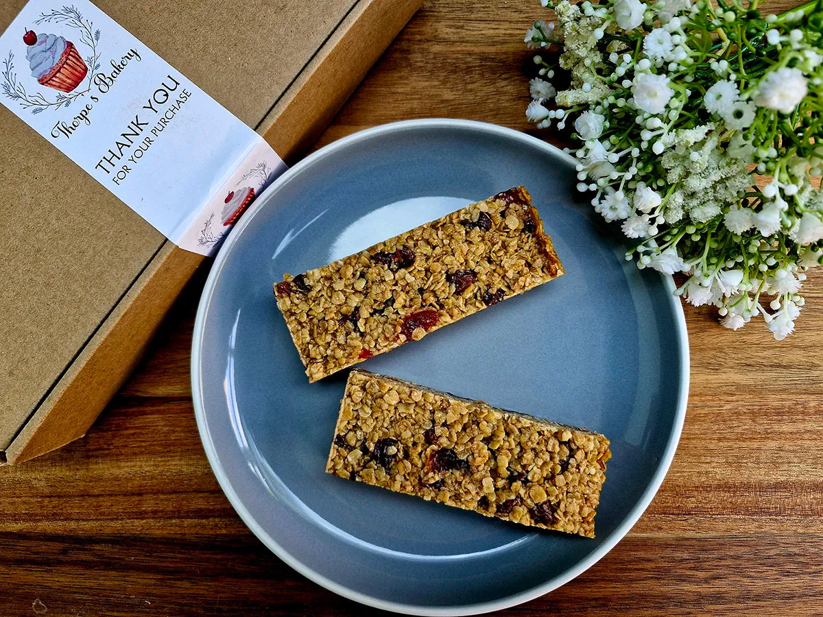 Two golden cherry & sultana flapjack slices on a plate beside Thorpe’s Bakery treat box.