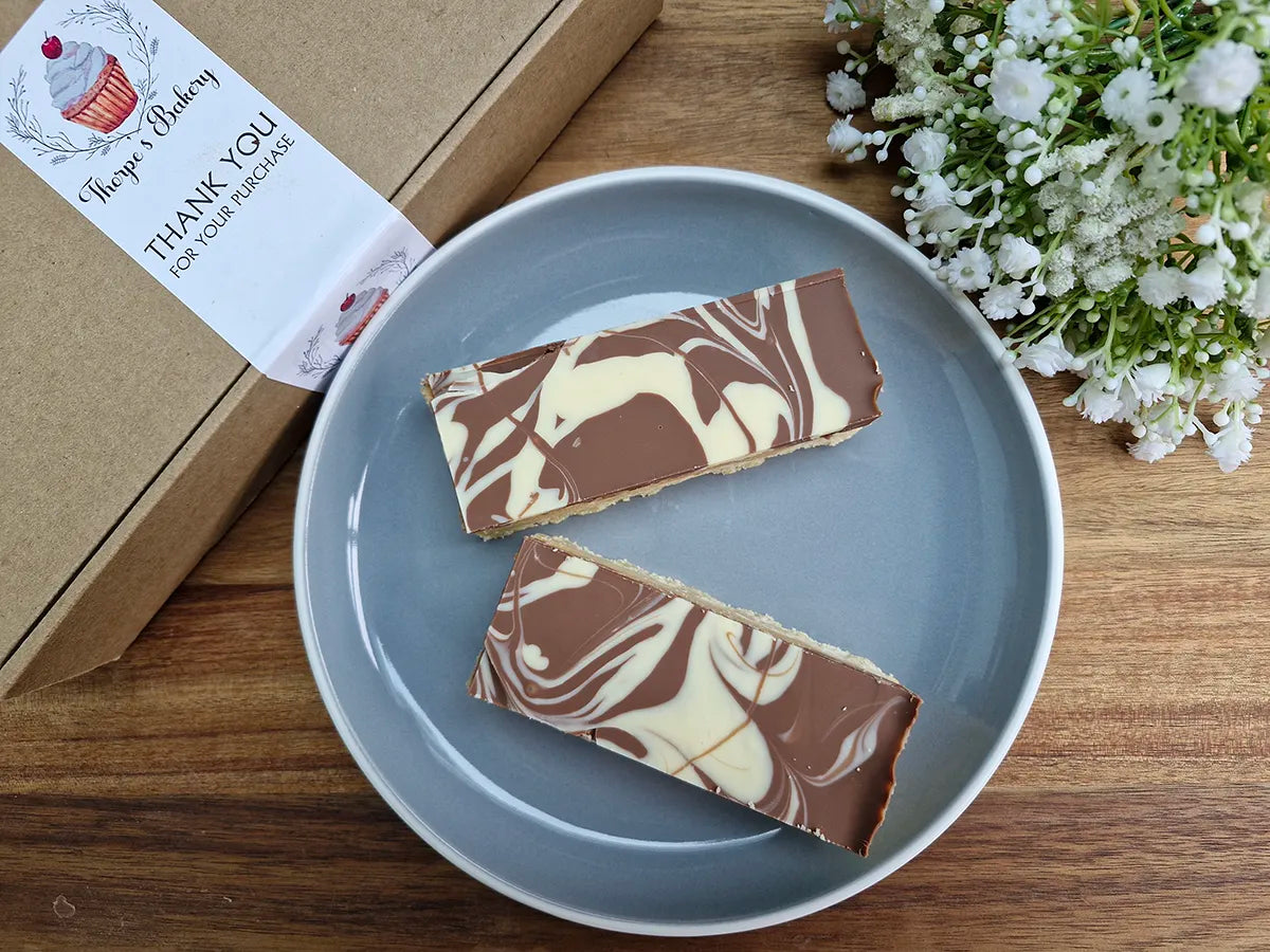 Two millionaire’s shortbread slices with marbled chocolate topping beside a Thorpe’s Bakery treat box.