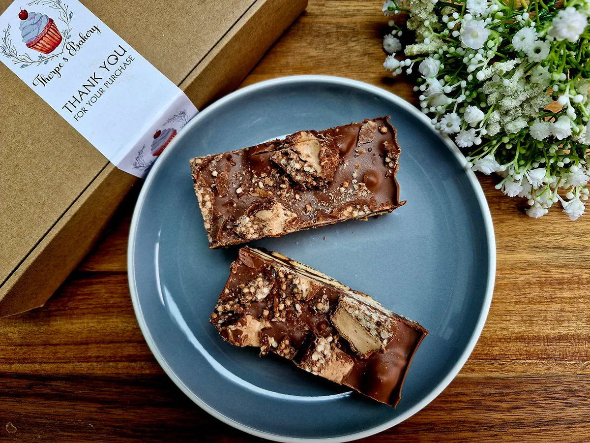 Two large double decker chocolate tiffin slices on a plate beside a Thorpe’s Bakery treat box.