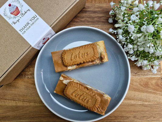 Two large Biscoff blondie slices on a plate beside a Thorpe’s Bakery treat box on a rustic wooden surface.
