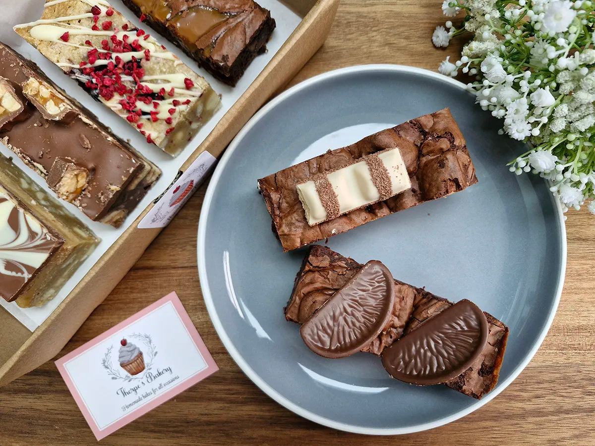 Assorted baked treats including chocolate orange brownies & millionaires shortbread arranged in a gift box.