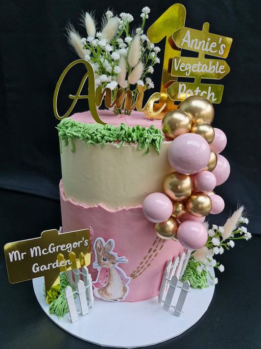 Two tier sponge cake topped with pink & yellow buttercream, personalised topper and colour coordinated decorations.