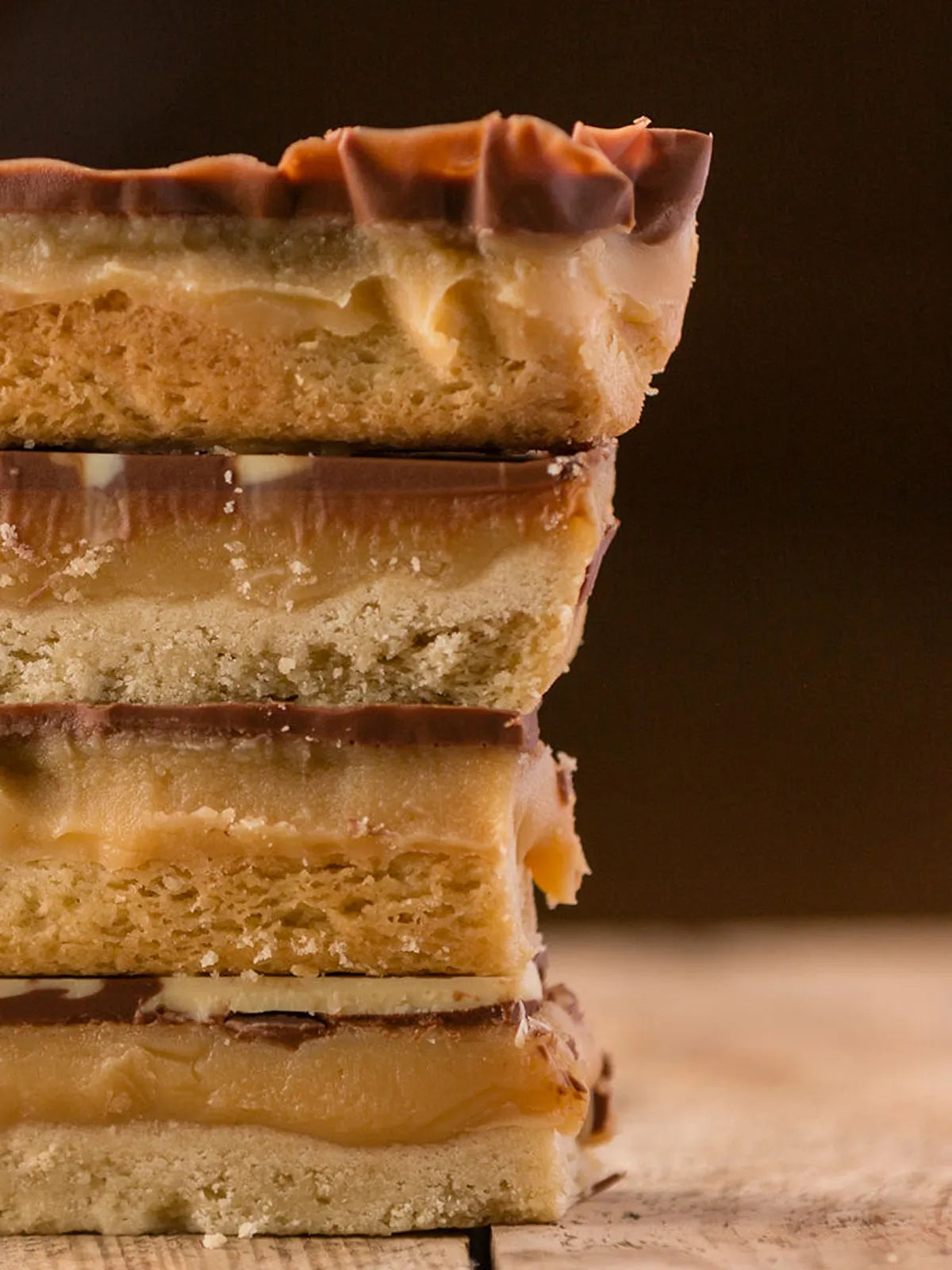 Four millionaires shortbread slices stacked on a rustic wooden surface.